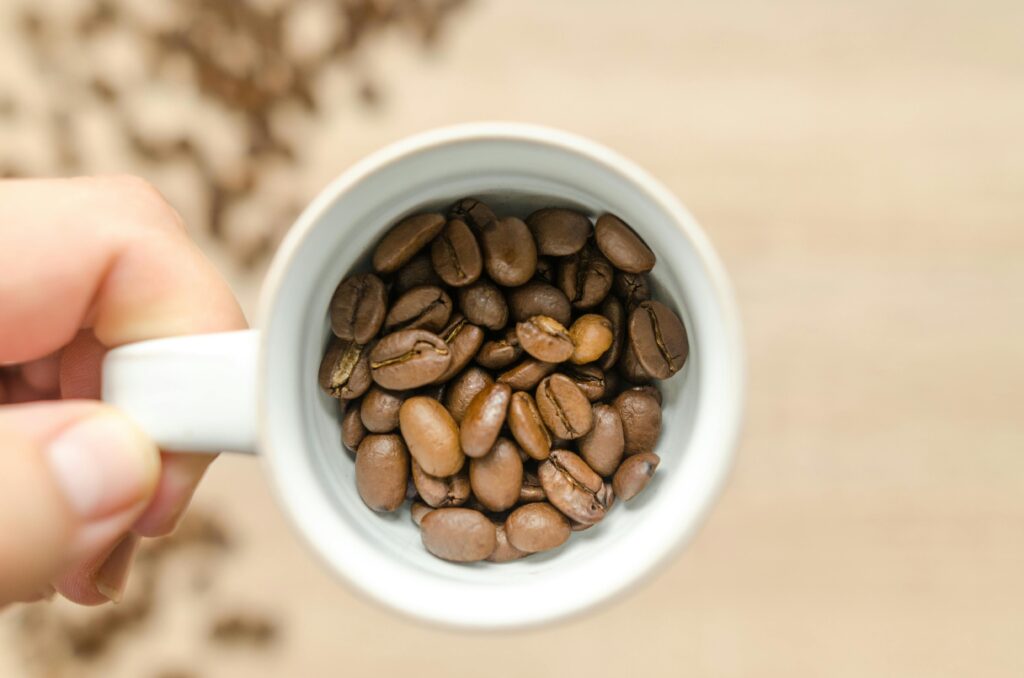 Hand holding a white cup filled with aromatic roasted coffee beans. Perfect for coffee lovers.