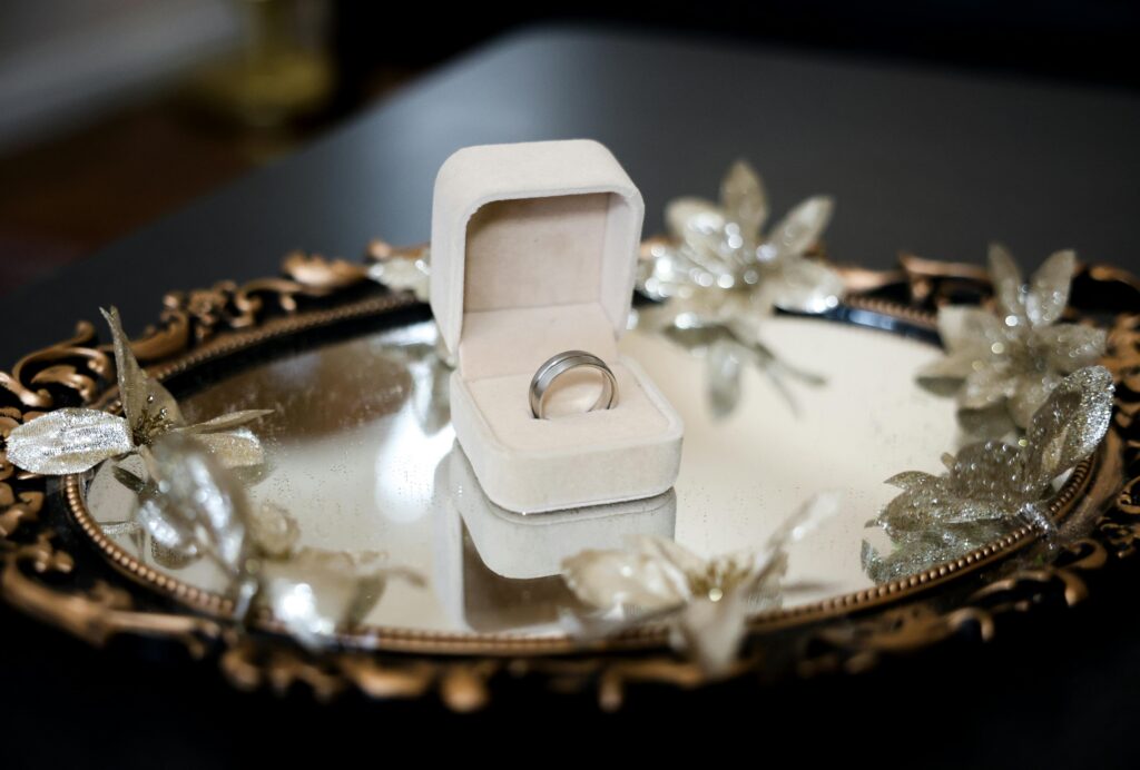 A silver engagement ring elegantly displayed in its box on a decorative mirror tray adorned with gold accents.
