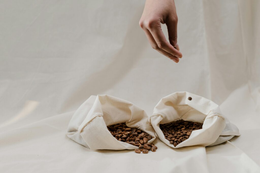 Minimalist image of coffee beans in canvas bags with a hand showcasing sustainability.