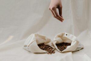 Minimalist image of coffee beans in canvas bags with a hand showcasing sustainability.