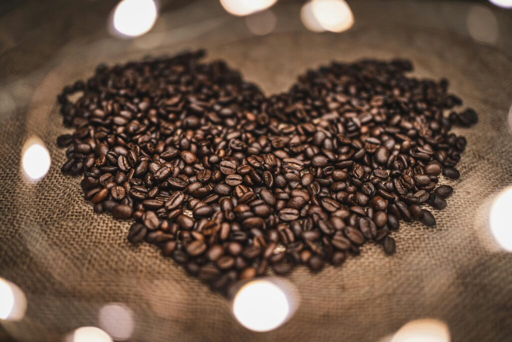 A creative display of roasted coffee beans arranged in a heart shape on burlap for coffee lovers.